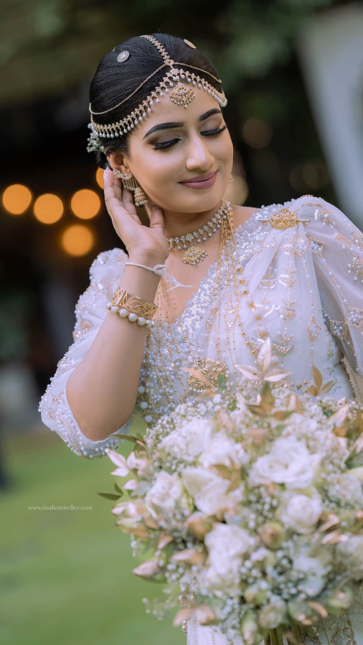 A bride in a pearl headpiece touching her earring, cradling a bouquet of white roses