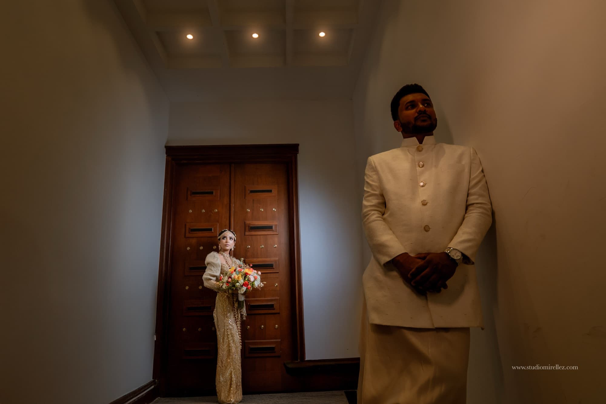 A bride with a bouquet and a groom in cream attire in a moody architectural portrait